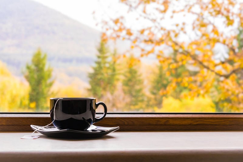 A dark ceramic coffee cup and saucer sit on a wooden windowsill.